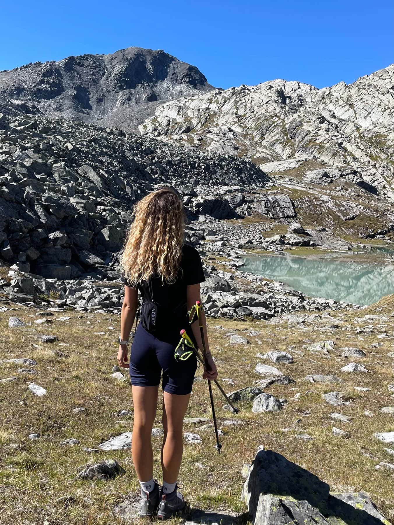 Lisa de dos, bâtons de marche en main, face à un lac glaciaire sur le sentier des lacs de Verbier