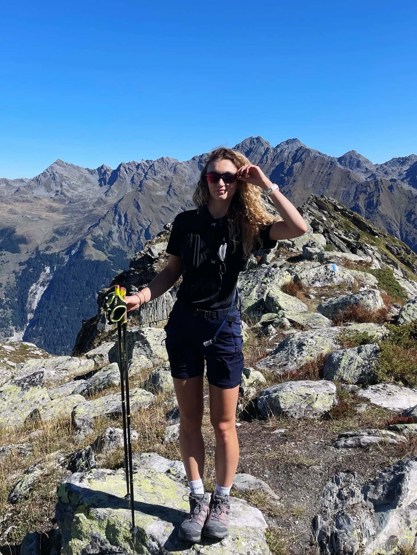 Lisa sur une arête rocheuse en Valais, bâtons de marche en main